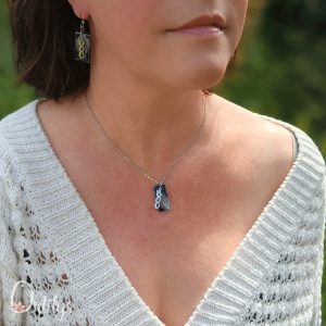 Un collier argenté, dont le médaillon rectangulaire a un fond noir, par dessus une papille argentée où il est écrit "boo" verticalement, et qui fait toute la hauteur du médaillon